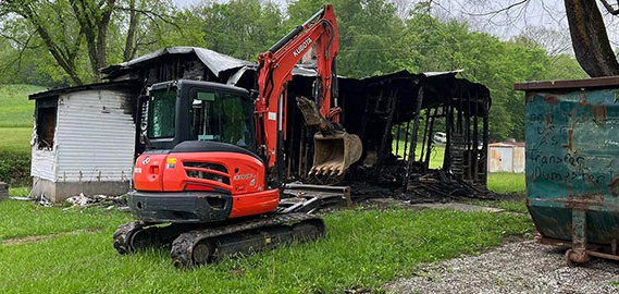 A hoe machine working on an old burned out house