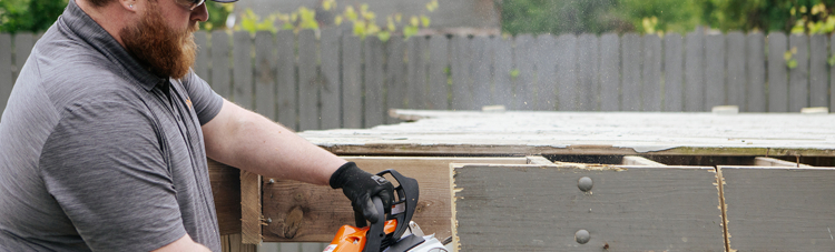 Worker cutting deck section with a chainsaw